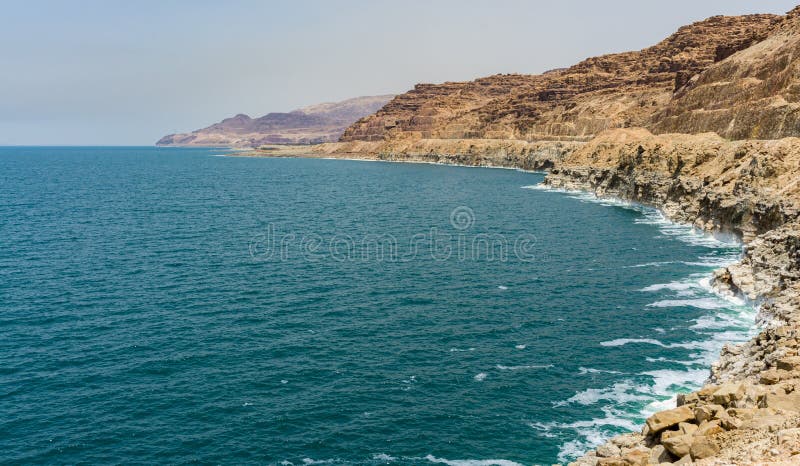 Beautiful cliffs cascade down into emerald water of Dead Sea. Salt crystals show in strips level of leaving water 2011 year. Dead Sea coastline in Jordan. Ecology theme. There is place for your text. Beautiful cliffs cascade down into emerald water of Dead Sea. Salt crystals show in strips level of leaving water 2011 year. Dead Sea coastline in Jordan. Ecology theme. There is place for your text