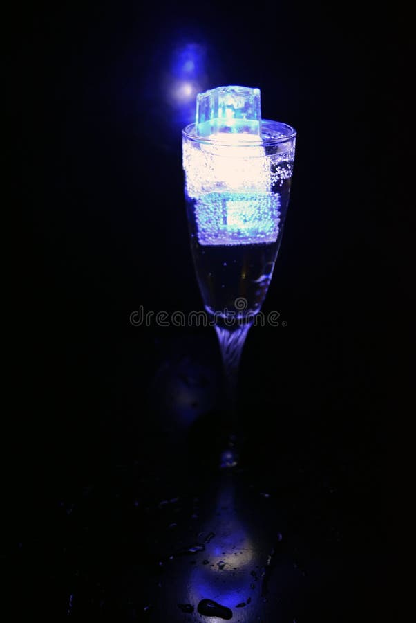 Hermosos y luminosos cubos de hielo azul brillante flotando en una copa de champán con una copa. imágenes de archivo libres de regalías