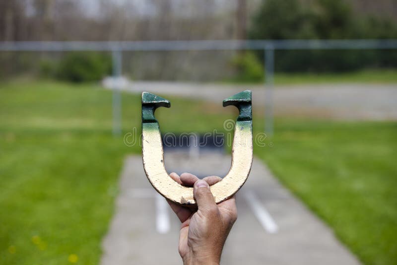 Player lines up to pitch a horseshoe in an outdoor court, hand and horseshoe in focus. Player lines up to pitch a horseshoe in an outdoor court, hand and horseshoe in focus