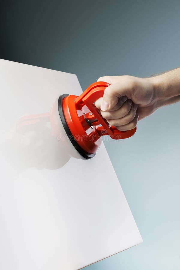 Man lifting a white ceramic tile using a vacuum suction cup tool aka dent puller. Man lifting a white ceramic tile using a vacuum suction cup tool aka dent puller.