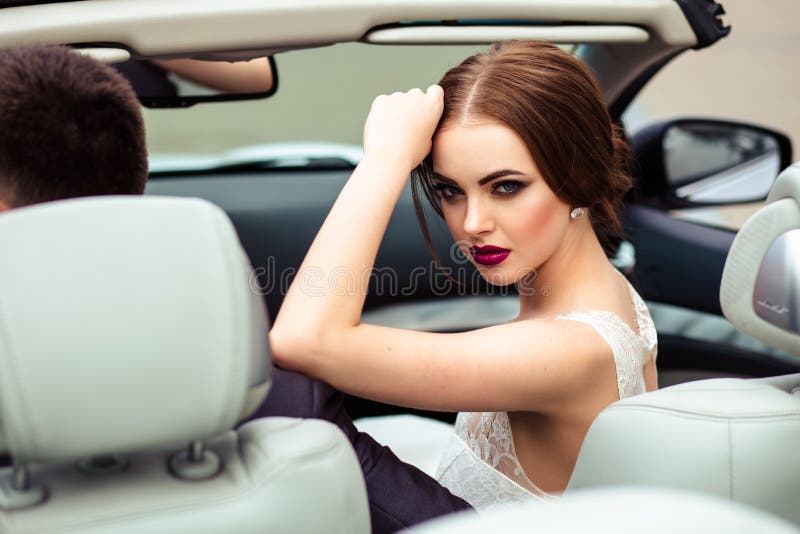 Herrliche Braut mit Modemake-up und -frisur in einem Luxushochzeitskleid mit hübschem Bräutigam nahe weißem Cabrioletauto stockbild Herrliche Braut mit Modemake-up und -frisur in einem Luxushochzeitskleid mit hübschem Bräutigam nahe weißem Cabrioletauto stockbild