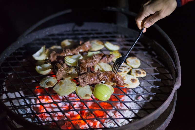Herstellung des Grills nachts Menschliche Hand, welche die Gabel vereinbart Würste, Kartoffeln und Zwiebeln auf Grill hält Braai, stockbilder Herstellung des Grills nachts Menschliche Hand, welche die Gabel vereinbart Würste, Kartoffeln und Zwiebeln auf Grill hält Braai, stockbilder