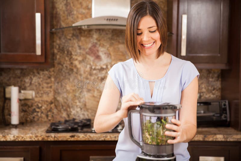 Happy young woman using a blender to make a healthy green juice at home. Happy young woman using a blender to make a healthy green juice at home