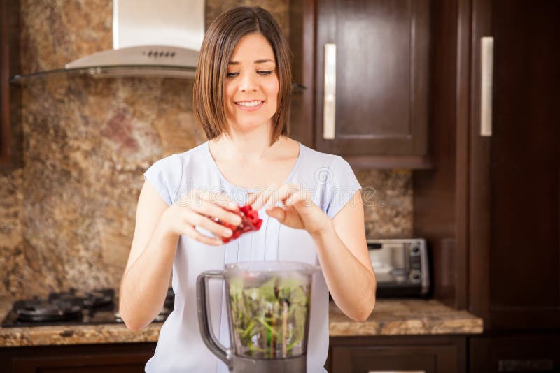 Cute young woman pouring some berries into a blender and making a healthy juice in the morning. Cute young woman pouring some berries into a blender and making a healthy juice in the morning