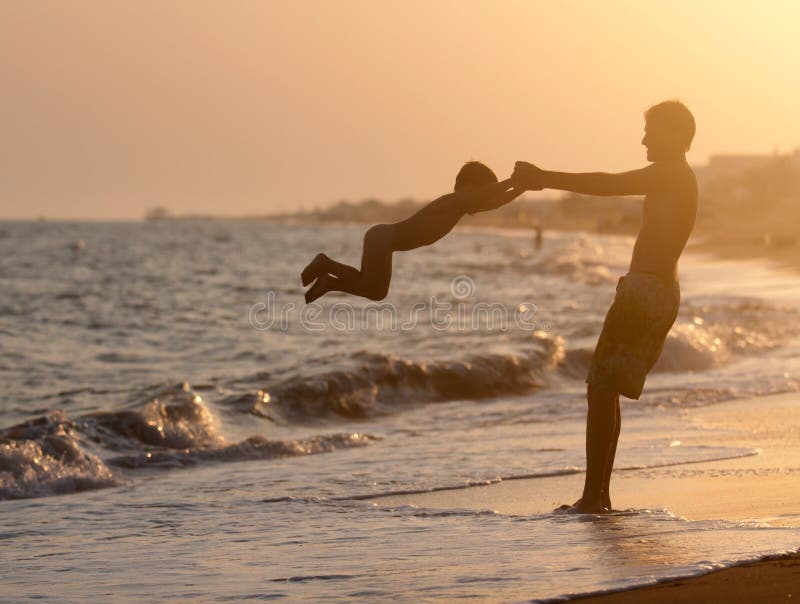 Hervorbringen Sie Spiele mit seinem Sohn auf dem Strand am Sonnenuntergang lizenzfreie stockfotos Hervorbringen Sie Spiele mit seinem Sohn auf dem Strand am Sonnenuntergang lizenzfreie stockfotos