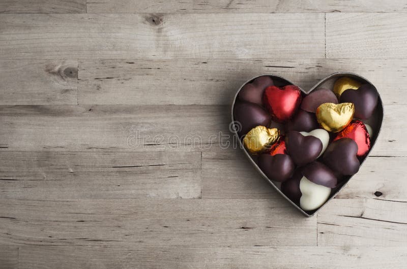 Overhead shot of open heart shaped box containing a variety of home made chocolates on old, worn light wood plank table. Overhead shot of open heart shaped box containing a variety of home made chocolates on old, worn light wood plank table.