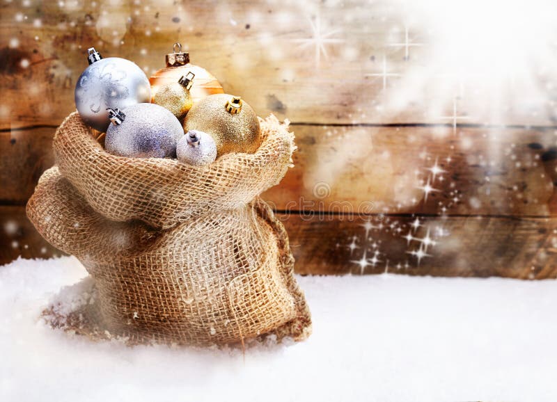 Hessian sack filled to overflowing with gold and silver Christmas baubles resting on snow in front of a rustic wooden wall with twinkling snowflakes and copyspace. Hessian sack filled to overflowing with gold and silver Christmas baubles resting on snow in front of a rustic wooden wall with twinkling snowflakes and copyspace