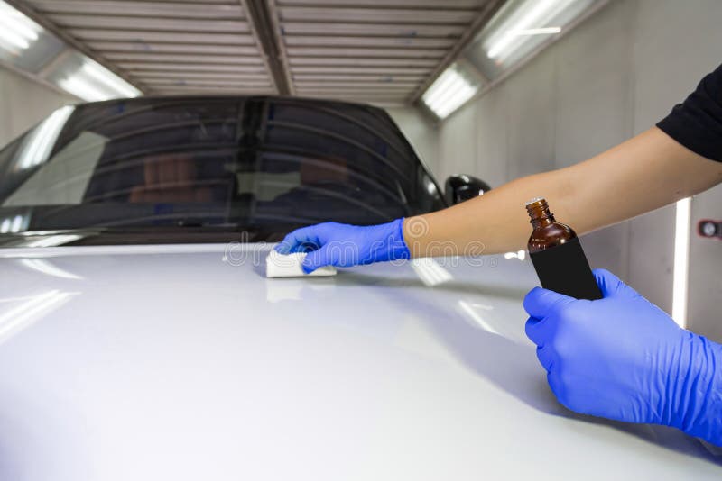 Het aanbrengen van een nano-keramische deklaag op de kap van de witte auto door een mannelijke werknemer met een spons en een che