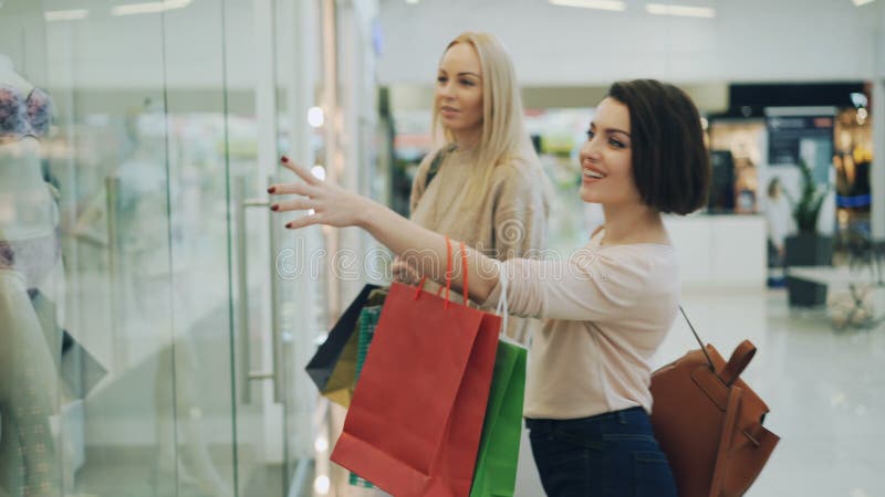 Het aantrekkelijke blonde winkelt met haar vrij vrouwelijke vriend die en het glimlachen in wandelgalerij babbelen lopen dan beki