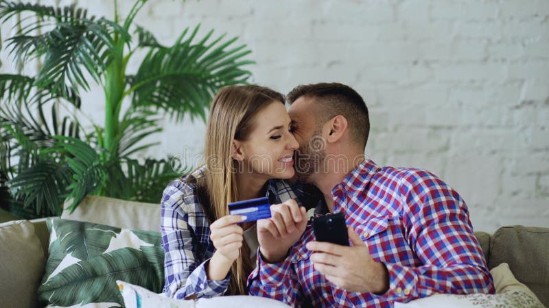 Het aantrekkelijke jonge paar met smartphone en de creditcard die op Internet winkelen zitten thuis op laag in woonkamer royalty-vrije stock foto's Het aantrekkelijke jonge paar met smartphone en de creditcard die op Internet winkelen zitten thuis op laag in woonkamer royalty-vrije stock foto's