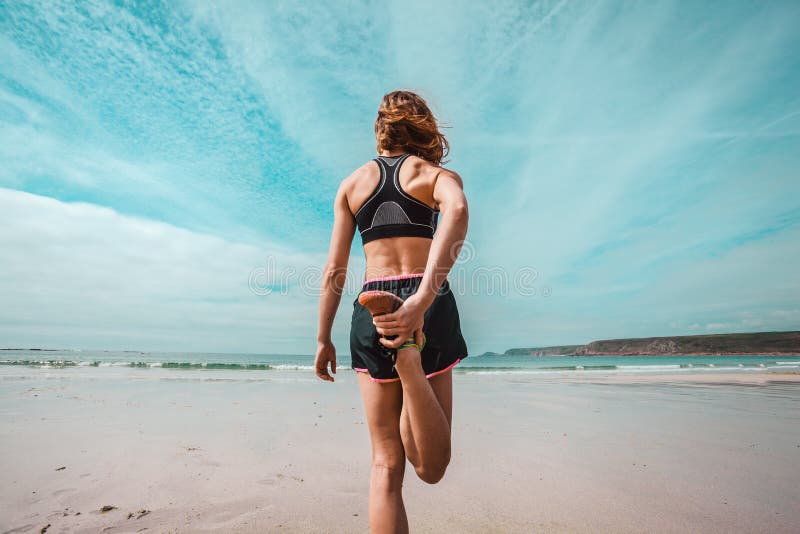 An athletic young woman is stretching her leg on the beach. An athletic young woman is stretching her leg on the beach