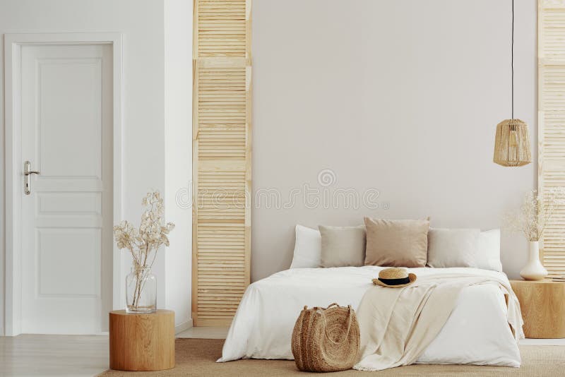 Het bed van de koningsgrootte met wit en beige beddegoed in modieuze slaapkamer, exemplaarruimte op lege muur