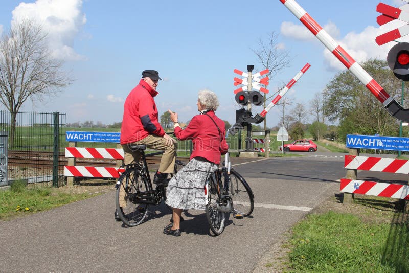 Het bejaarde paar op fietsen wacht bij spoorwegovergang