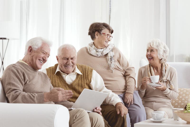 Elderly friends relaxing at day-care center chatting and using a laptop. Elderly friends relaxing at day-care center chatting and using a laptop