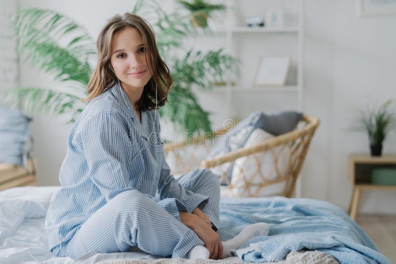 Het binnenschot van vrij donkere haired vrouw zit gekruiste benen op bed, gekleed in nighclothes, witte sokken, bekijkt direcltly royalty-vrije stock afbeelding Het binnenschot van vrij donkere haired vrouw zit gekruiste benen op bed, gekleed in nighclothes, witte sokken, bekijkt direcltly royalty-vrije stock afbeelding