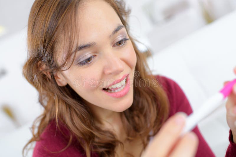 Het blije jonge vrouw te weten komen vloeit de zitting van de pregancytest op bank voort stock fotografie Het blije jonge vrouw te weten komen vloeit de zitting van de pregancytest op bank voort stock fotografie