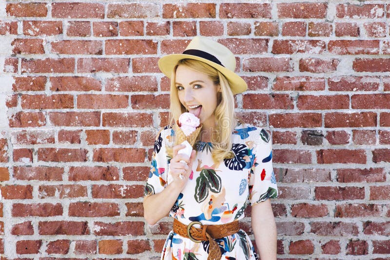 Het blonde Kaukasische Meisje likt Roomijs tegen een Bakstenen muurkegel Fedora Hat stock foto's Het blonde Kaukasische Meisje likt Roomijs tegen een Bakstenen muurkegel Fedora Hat stock foto's
