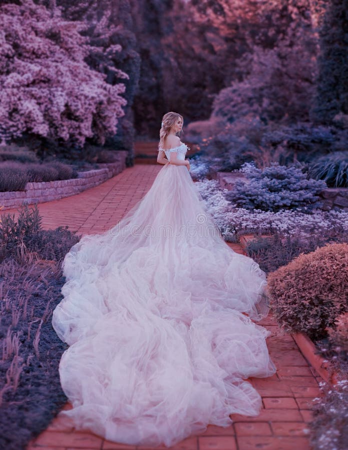 Het blonde, met een mooi elegant kapsel, loopt in een fabelachtige bloeiende tuin Prinses in een luxueuze lichtrose kleding stock foto's Het blonde, met een mooi elegant kapsel, loopt in een fabelachtige bloeiende tuin Prinses in een luxueuze lichtrose kleding stock foto's