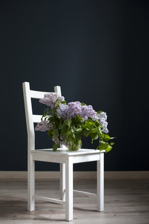 Het boeket van lilac takjes in een transparante groene kruik op de witte stoel als decoratie van binnenland tegenovergesteld van royalty-vrije stock fotografie Het boeket van lilac takjes in een transparante groene kruik op de witte stoel als decoratie van binnenland tegenovergesteld van royalty-vrije stock fotografie
