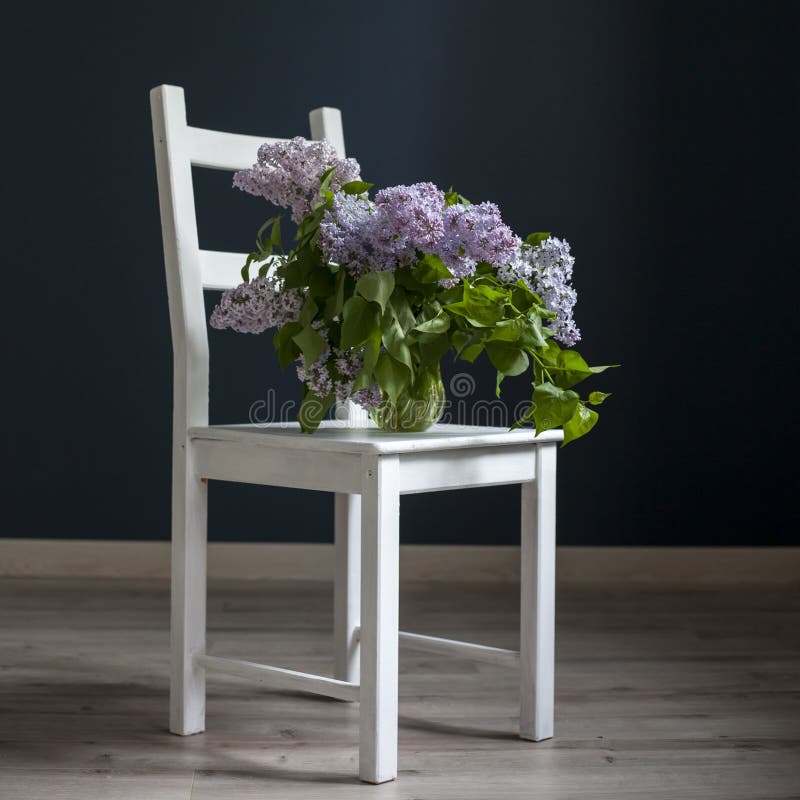 Het boeket van lilac takjes in een transparante groene kruik op de witte stoel als decoratie van binnenland tegenovergesteld van stock afbeeldingen Het boeket van lilac takjes in een transparante groene kruik op de witte stoel als decoratie van binnenland tegenovergesteld van stock afbeeldingen