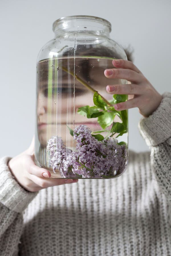 Het boeket van lilac takjes in een transparante kruik op witte stoel als decoratie van binnenland Het meisje zit op het venster royalty-vrije stock afbeeldingen Het boeket van lilac takjes in een transparante kruik op witte stoel als decoratie van binnenland Het meisje zit op het venster royalty-vrije stock afbeeldingen