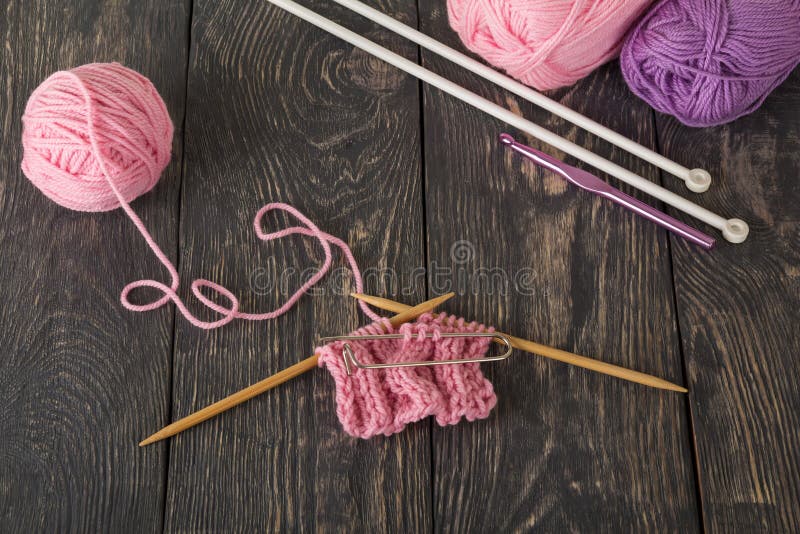 Het breien van een roze sjaal, gemengd garen op donkere raad stock afbeelding Het breien van een roze sjaal, gemengd garen op donkere raad stock afbeelding
