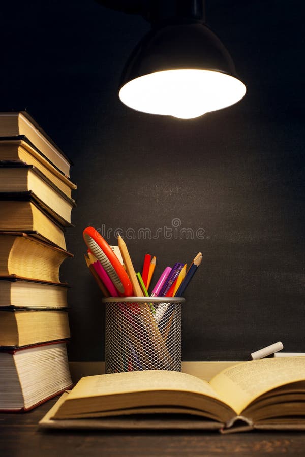 Het bureau van de leraar of een arbeider, waarop het schrijfgerei ligt, boeken, in de avond onder de lamp Spatie voor tekst of stock fotografie Het bureau van de leraar of een arbeider, waarop het schrijfgerei ligt, boeken, in de avond onder de lamp Spatie voor tekst of stock fotografie