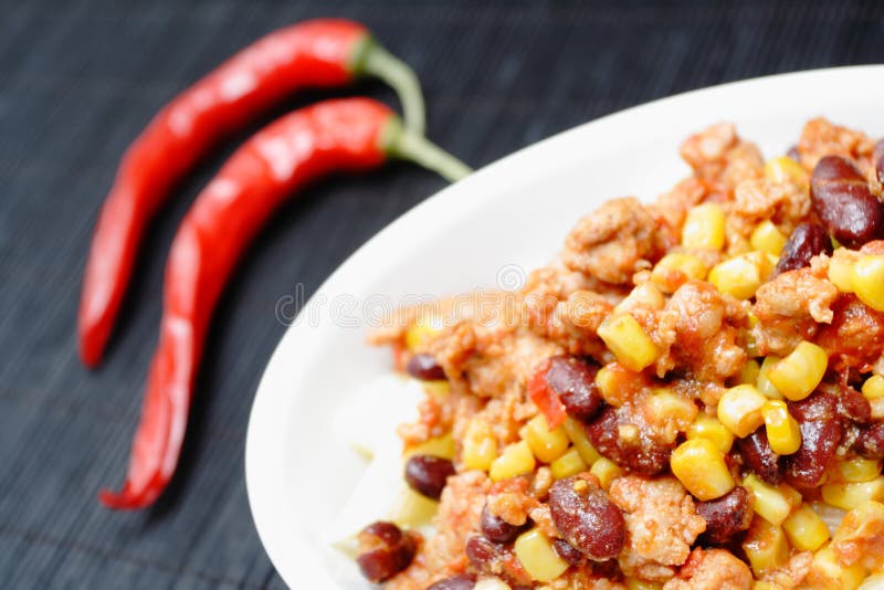 Mexican food chili con carne and two red peppers on a white plate. Mexican food chili con carne and two red peppers on a white plate