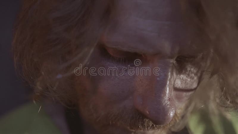 Het close-up van de langharige smid in smeedt De camerabenaderingen en de smidsdraaien naar de oven