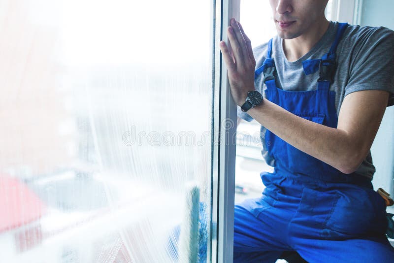 Het close-up van een mens in eenvormige en blauwe handschoenen wast vensters met vensterschraper De professionele huis schoonmake stock foto's Het close-up van een mens in eenvormige en blauwe handschoenen wast vensters met vensterschraper De professionele huis schoonmake stock foto's