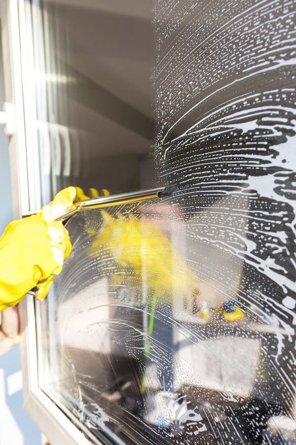 Het close-up van een vrouw in eenvormige en gele handschoenen wast vensters met vensterschraper Het professionele huis schoonmake royalty-vrije stock fotografie Het close-up van een vrouw in eenvormige en gele handschoenen wast vensters met vensterschraper Het professionele huis schoonmake royalty-vrije stock fotografie