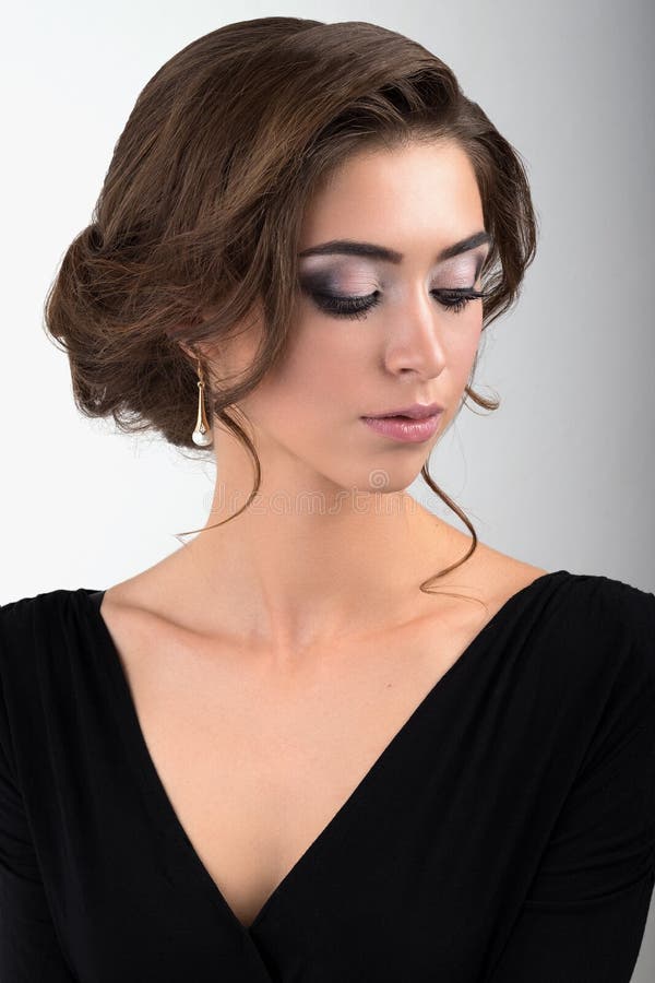 Het close-upportret van brunette met avondmake-up en verzameld haar in een zwarte kleding met ogen sloot status op een lichte bac royalty-vrije stock fotografie Het close-upportret van brunette met avondmake-up en verzameld haar in een zwarte kleding met ogen sloot status op een lichte bac royalty-vrije stock fotografie