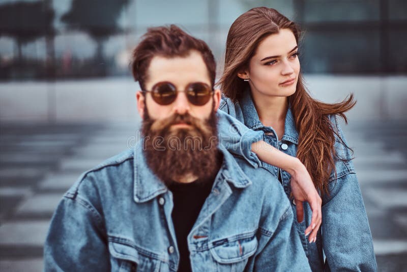 Het close-upportret van een hipsterpaar van een brutaal gebaard mannetje in zonnebril en zijn meisje kleedde zich in jeansjasjes royalty-vrije stock foto's Het close-upportret van een hipsterpaar van een brutaal gebaard mannetje in zonnebril en zijn meisje kleedde zich in jeansjasjes royalty-vrije stock foto's