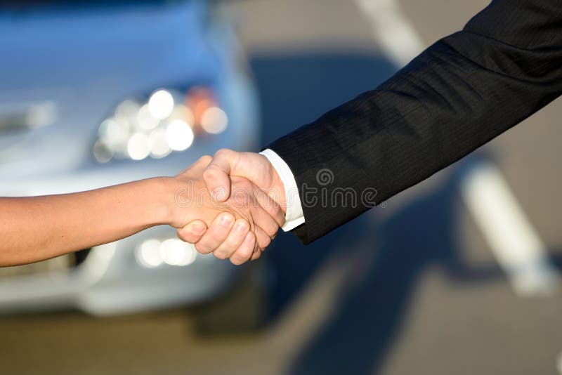 Man and woman closing a car sale agreement with a handshake. Salesman and buyer shaking hands. Man and woman closing a car sale agreement with a handshake. Salesman and buyer shaking hands