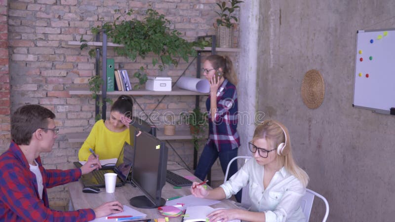 Het dagelijkse werk in bureau, jonge werknemers werkt bij computers en maakt verslagen zittend bij lijst in een modern bureau