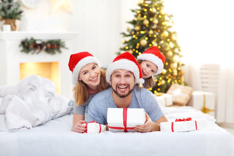 Happy family mother father and child on Christmas morning in bed in pajamas open gifts. Happy family mother father and child on Christmas morning in bed in pajamas open gifts