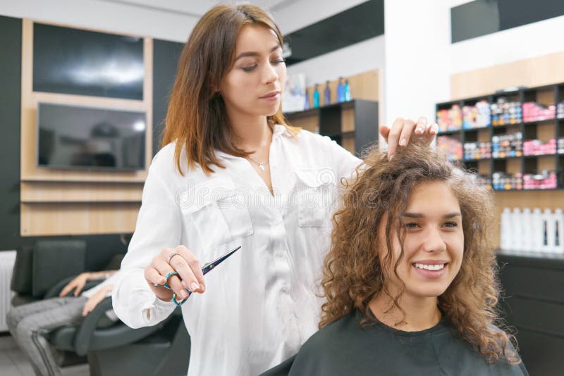 Het doen van nieuwe hairdress voor glimlachende krullende vrouwelijke cliënt royalty-vrije stock afbeelding Het doen van nieuwe hairdress voor glimlachende krullende vrouwelijke cliënt royalty-vrije stock afbeelding