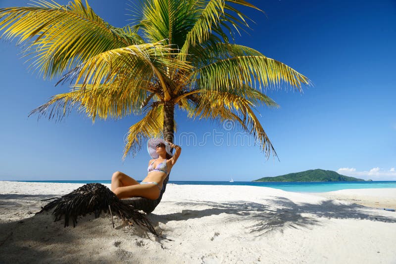 Het dromen vrouwenzitting op het strand onder een palm op een beaut royalty-vrije stock foto Het dromen vrouwenzitting op het strand onder een palm op een beaut royalty-vrije stock foto