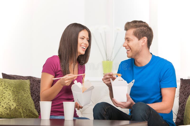 Beautiful couple eating Asian food from food containers and smiling. Beautiful couple eating Asian food from food containers and smiling