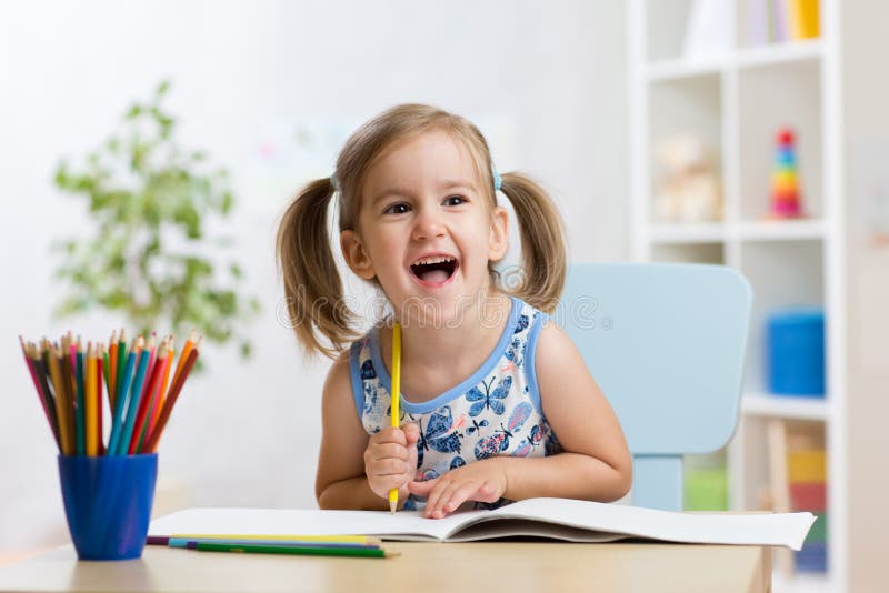 Het expressieve jong geitjemeisje trekt zitting bij lijst in ruimte in kinderdagverblijf stock foto Het expressieve jong geitjemeisje trekt zitting bij lijst in ruimte in kinderdagverblijf stock foto