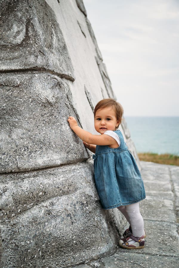 Het gelukkige kleine babymeisje in jeans kleedt status dichtbij aan de muur van de oude vuurtoren royalty-vrije stock foto's Het gelukkige kleine babymeisje in jeans kleedt status dichtbij aan de muur van de oude vuurtoren royalty-vrije stock foto's