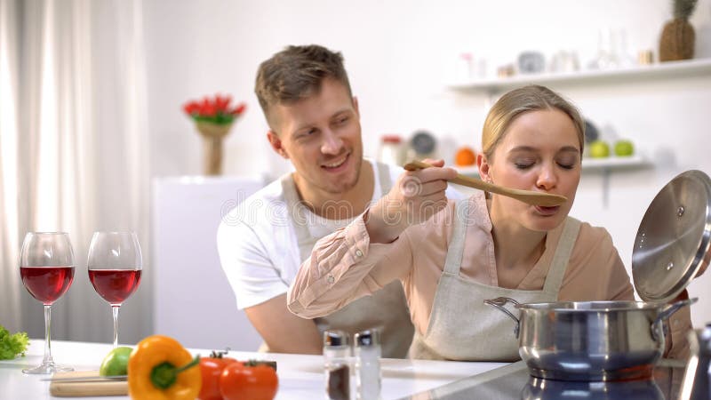 Het gelukkige paar koken samen in keuken, vrouwelijke proevende soep, gezond voedsel stock foto Het gelukkige paar koken samen in keuken, vrouwelijke proevende soep, gezond voedsel stock foto