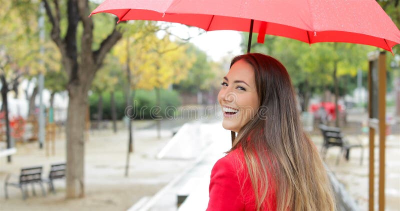 Het gelukkige vrouw glimlachen die camera onder de regen bekijken