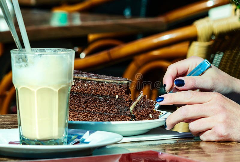 Het genieten van van smakelijke cake en Latte-macchiato in de zonneschijn stock fotografie Het genieten van van smakelijke cake en Latte-macchiato in de zonneschijn stock fotografie