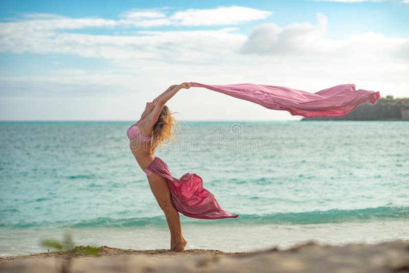 Het geschikte en sportieve jonge meisje stellen op een strand met roze vliegende zijde stock fotografie Het geschikte en sportieve jonge meisje stellen op een strand met roze vliegende zijde stock fotografie