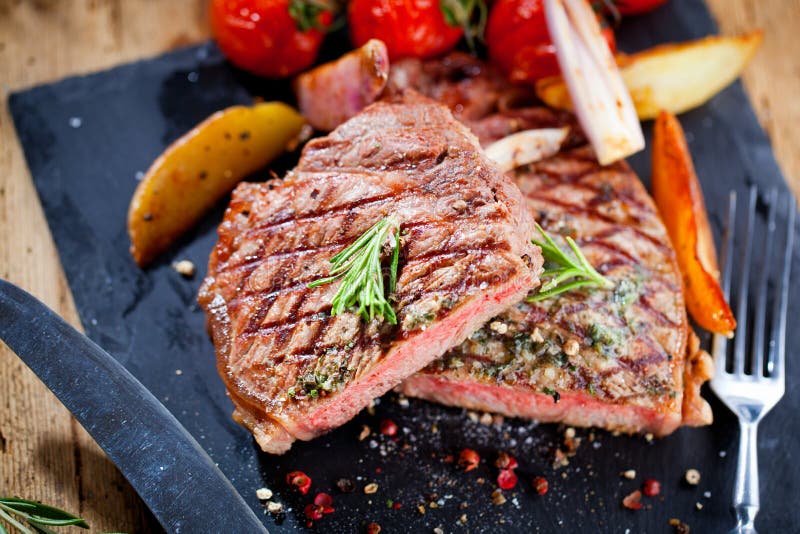 Het gesneden geroosterde lapje vlees Striploin van de vleesbarbecue met mes en vorkgravure plaatste op zwarte steenlei royalty-vrije stock afbeeldingen Het gesneden geroosterde lapje vlees Striploin van de vleesbarbecue met mes en vorkgravure plaatste op zwarte steenlei royalty-vrije stock afbeeldingen