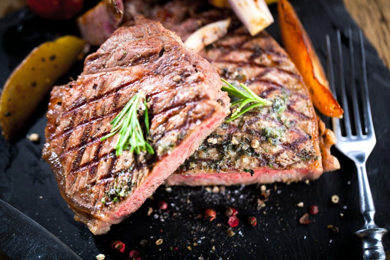 Het gesneden geroosterde lapje vlees Striploin van de vleesbarbecue met mes en vorkgravure plaatste op zwarte steenlei stock foto's Het gesneden geroosterde lapje vlees Striploin van de vleesbarbecue met mes en vorkgravure plaatste op zwarte steenlei stock foto's