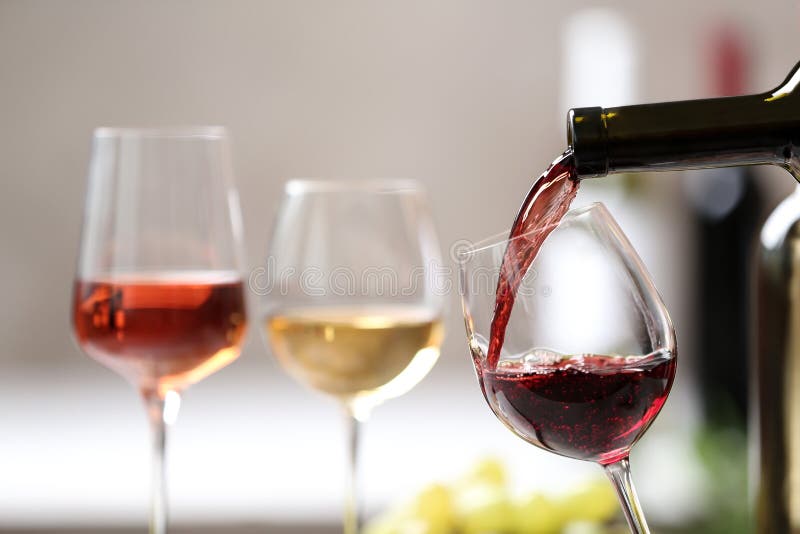 Pouring red wine from bottle into glass on blurred background. Space for text. Pouring red wine from bottle into glass on blurred background. Space for text