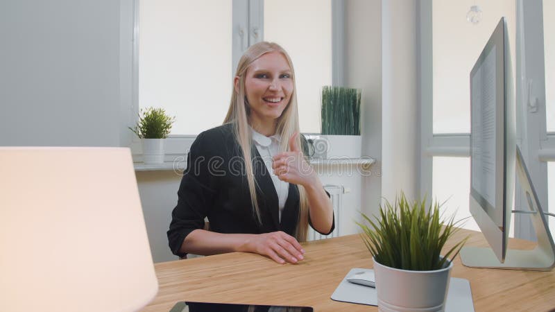 Het glimlachen het bedrijfsvrouw tonen beduimelt omhoog Vrolijk jong blond wijfje in elegante kostuumzitting in bureau bij bureau