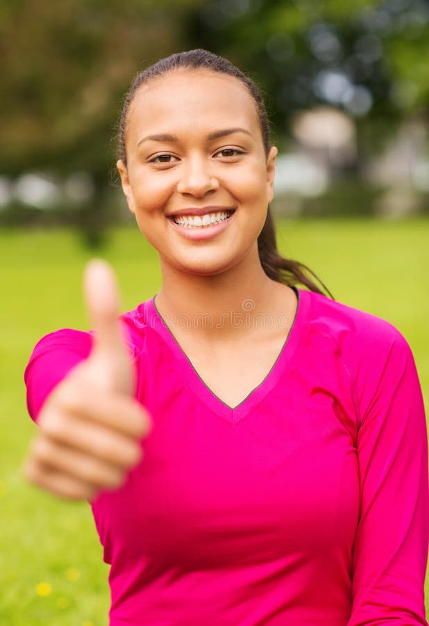 Fitness, park, happiness and people concept - portrait of smiling african american woman showing thumbs up outdoors. Fitness, park, happiness and people concept - portrait of smiling african american woman showing thumbs up outdoors.